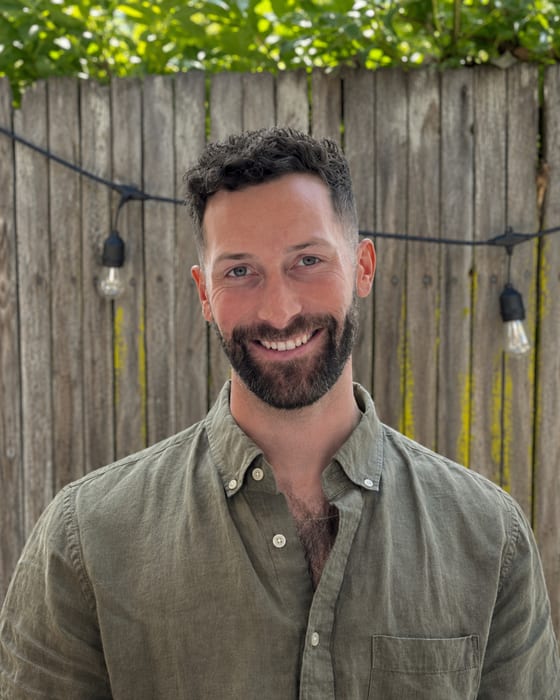 Ben Siverly, smiling, in front of a wooden fence draped with greenery and string lights